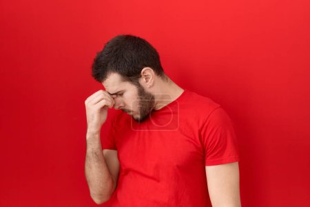 Foto de Hombre hispano joven con camiseta roja casual cansado frotando la nariz y los ojos sintiendo fatiga y dolor de cabeza. concepto de estrés y frustración. - Imagen libre de derechos