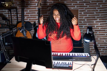 Téléchargez les photos : Plus taille femme hispanique jouant du piano au studio de musique célébrant surpris et étonnés par le succès avec les bras levés et les yeux ouverts. concept gagnant. - en image libre de droit