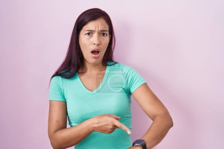Photo for Young hispanic woman standing over pink background in hurry pointing to watch time, impatience, upset and angry for deadline delay - Royalty Free Image