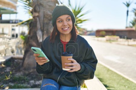 Téléchargez les photos : Jeune belle femme hispanique utilisant smartphone boire du café au parc - en image libre de droit