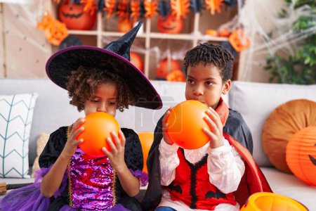 Photo for Adorable african american boy and girl having halloween party inflating balloon at home - Royalty Free Image