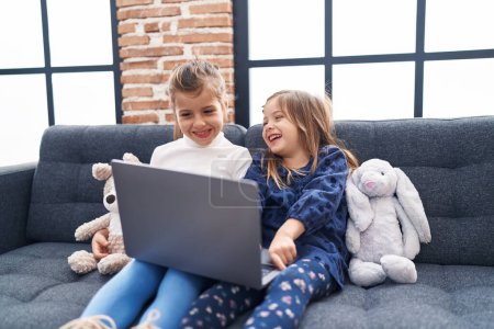 Photo for Adorable girls using laptop sitting on sofa at home - Royalty Free Image