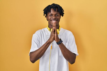 Photo for Young african man with dreadlocks standing over yellow background praying with hands together asking for forgiveness smiling confident. - Royalty Free Image