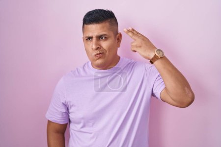 Foto de Young hispanic man standing over pink background shooting and killing oneself pointing hand and fingers to head like gun, suicide gesture. - Imagen libre de derechos