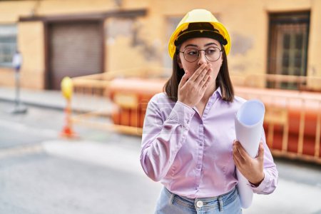Photo for Hispanic girl wearing architect hardhat at construction site covering mouth with hand, shocked and afraid for mistake. surprised expression - Royalty Free Image