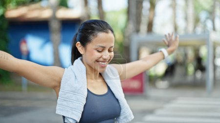 Foto de Joven mujer hispana hermosa usando ropa deportiva con los brazos abiertos sonriendo en la calle - Imagen libre de derechos