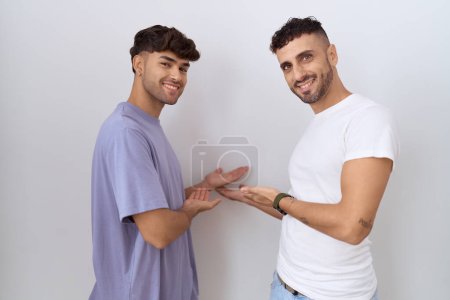 Foto de Homosexual pareja gay de pie sobre blanco fondo invitando a entrar sonriendo natural con la mano abierta - Imagen libre de derechos