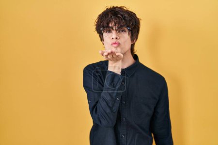 Photo for Young man wearing glasses over yellow background looking at the camera blowing a kiss with hand on air being lovely and sexy. love expression. - Royalty Free Image