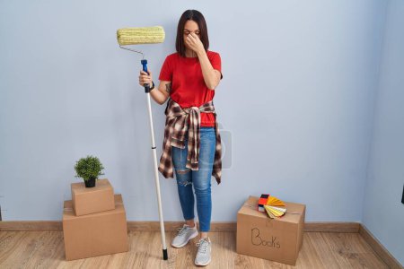 Photo for Young hispanic woman painting home walls with paint roller tired rubbing nose and eyes feeling fatigue and headache. stress and frustration concept. - Royalty Free Image