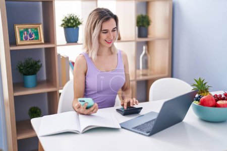 Photo for Young woman using smartphone and calculator studying at home - Royalty Free Image