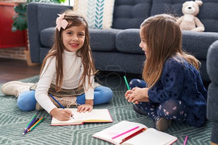 Téléchargez les photos : Adorables filles étudiants assis sur le sol dessin sur ordinateur portable à la maison - en image libre de droit