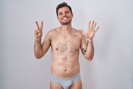 Téléchargez les photos : Jeune homme hispanique debout torse nu portant des sous-vêtements montrant et pointant vers le haut avec les doigts numéro sept tout en souriant confiant et heureux. - en image libre de droit