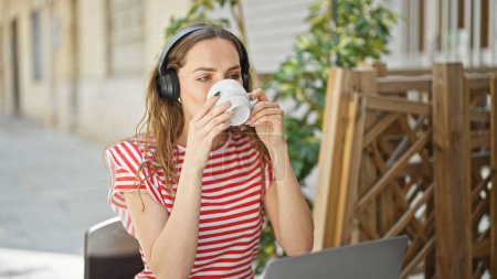 Téléchargez les photos : Jeune femme blonde écoutant de la musique boire du café sur la terrasse du café - en image libre de droit