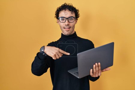 Téléchargez les photos : Hispanique homme travaillant en utilisant ordinateur portable souriant heureux pointage avec la main et le doigt - en image libre de droit