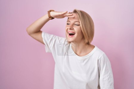 Photo for Young caucasian woman standing over pink background very happy and smiling looking far away with hand over head. searching concept. - Royalty Free Image