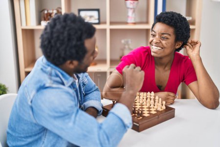 Téléchargez les photos : Africain américain homme et femme couple jouer aux échecs assis sur la table à la maison - en image libre de droit