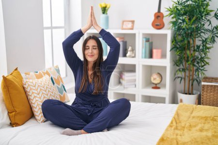 Foto de Joven hermosa mujer hispana haciendo ejercicio de yoga sentada en la cama en el dormitorio - Imagen libre de derechos