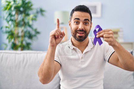 Photo for Young hispanic man with beard holding purple ribbon awareness surprised with an idea or question pointing finger with happy face, number one - Royalty Free Image