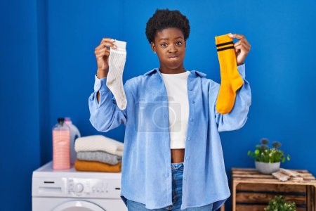 Téléchargez les photos : Femme afro-américaine tenant des chaussettes propres et sales gonflant les joues avec un visage drôle. bouche gonflée d'air, attrapant l'air. - en image libre de droit