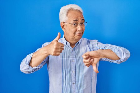 Photo for Hispanic senior man wearing glasses doing thumbs up and down, disagreement and agreement expression. crazy conflict - Royalty Free Image