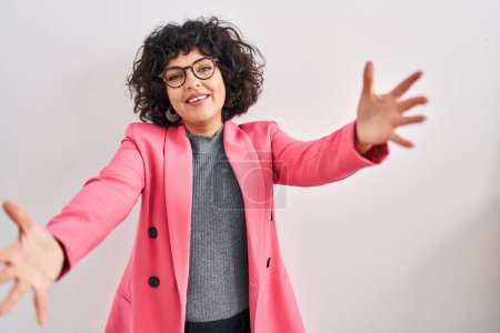 Photo for Hispanic woman with curly hair standing over isolated background looking at the camera smiling with open arms for hug. cheerful expression embracing happiness. - Royalty Free Image