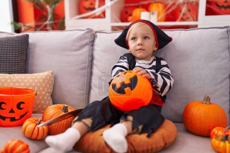 Photo for Adorable caucasian boy wearing pirate costume holding sweet on pumpkin basket at home - Royalty Free Image