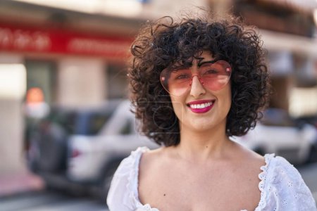 Foto de Joven mujer de Oriente Medio sonriendo confiado usando gafas de sol de corazón en la calle - Imagen libre de derechos