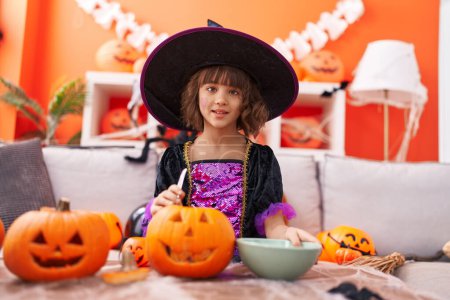 Téléchargez les photos : Adorable fille hispanique ayant fête d'Halloween tenant panier de citrouille à la maison - en image libre de droit