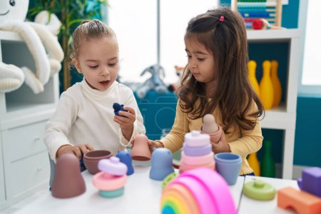 Foto de Adorables chicas jugando con bloques de construcción sentadas en la mesa en el jardín de infantes - Imagen libre de derechos
