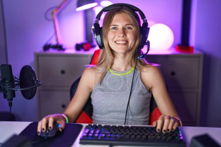 Téléchargez les photos : Femme caucasienne blonde jouant à des jeux vidéo avec écouteurs regardant positif et heureux debout et souriant avec un sourire confiant montrant les dents - en image libre de droit
