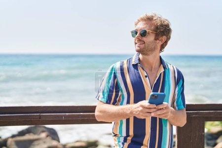 Foto de Joven turista sonriendo confiado usando teléfono inteligente en la playa - Imagen libre de derechos