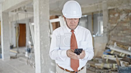 Téléchargez les photos : Architecte chevelu utilisant un smartphone regardant autour du chantier de construction - en image libre de droit