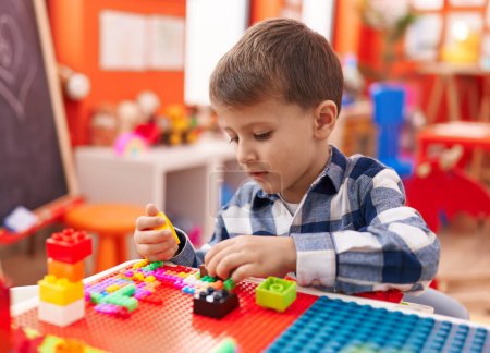 Foto de Adorable chico caucásico jugando con bloques de construcción sentado en la mesa en el jardín de infantes - Imagen libre de derechos
