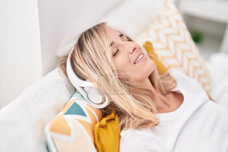 Téléchargez les photos : Young blonde woman listening to music lying on bed at bedroom - en image libre de droit
