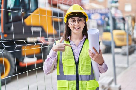 Photo for Hispanic girl wearing architect hardhat at construction site pointing finger to one self smiling happy and proud - Royalty Free Image