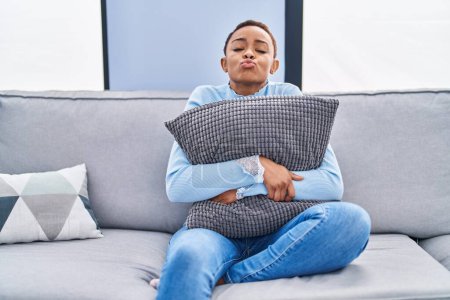 Photo for African american woman sitting on the sofa at home hugging pillow looking at the camera blowing a kiss being lovely and sexy. love expression. - Royalty Free Image