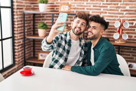 Téléchargez les photos : Jeune couple faire selfie par le smartphone assis sur la table à la maison - en image libre de droit