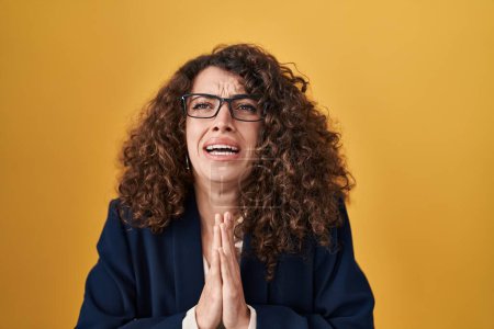 Photo for Hispanic woman with curly hair standing over yellow background begging and praying with hands together with hope expression on face very emotional and worried. begging. - Royalty Free Image