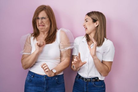 Photo for Hispanic mother and daughter wearing casual white t shirt over pink background disgusted expression, displeased and fearful doing disgust face because aversion reaction. - Royalty Free Image