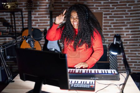 Téléchargez les photos : Plus taille hispanique femme jouant du piano au studio de musique pointant du doigt avec une idée réussie. Sorti et heureux. numéro un. - en image libre de droit