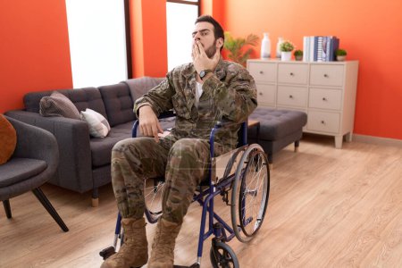 Foto de Joven soldado hispano herido sentado en silla de ruedas cubriendo la boca con la mano, sorprendido y temeroso de equivocarse. expresión sorprendida - Imagen libre de derechos