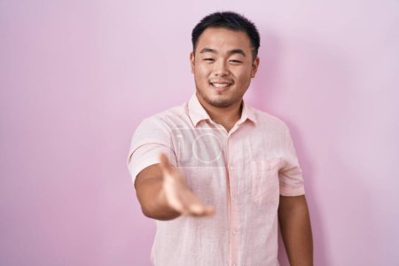 Téléchargez les photos : Chinois jeune homme debout sur fond rose souriant joyeuse offrant main de paume donnant assistance et acceptation. - en image libre de droit