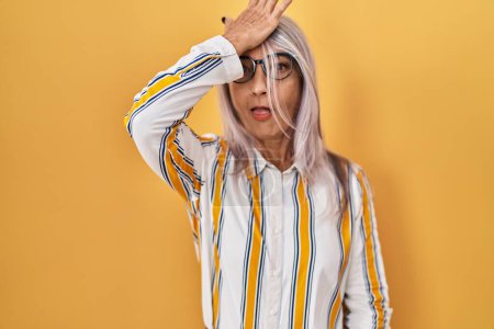 Photo for Middle age woman with grey hair standing over yellow background wearing glasses surprised with hand on head for mistake, remember error. forgot, bad memory concept. - Royalty Free Image