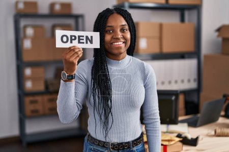 Photo for African american woman working at small business ecommerce holding open banner looking positive and happy standing and smiling with a confident smile showing teeth - Royalty Free Image