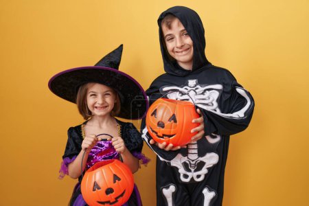 Foto de Adorable niño y niña con disfraz de halloween sosteniendo cesta de calabaza sobre fondo amarillo aislado - Imagen libre de derechos