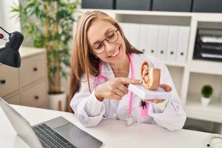 Téléchargez les photos : Jeune femme blonde gynécologue tenant le modèle anatomique de l'utérus à la clinique - en image libre de droit
