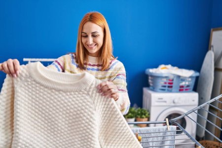 Foto de Joven mujer caucásica sonriendo confiado colgando ropa en tendedero en la sala de lavandería - Imagen libre de derechos