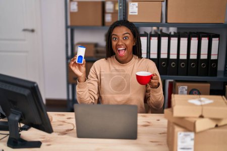 Téléchargez les photos : Jeune afro-américain avec des tresses travaillant dans une petite entreprise e-commerce boire un café avec édulcorant célébrer fou et étonné pour le succès avec les yeux ouverts hurlant excité. - en image libre de droit