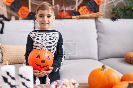 Photo for Adorable hispanic boy wearing skeleton costume holding pumpkin basket at home - Royalty Free Image