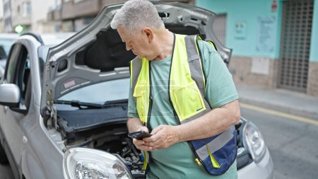 Photo for Middle age grey-haired man texting to insurance by smartphone for car breakdown at street - Royalty Free Image